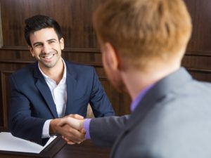 Portrait of young Caucasian businessman sitting in modern office and shaking hands with his partner after finishing meeting
